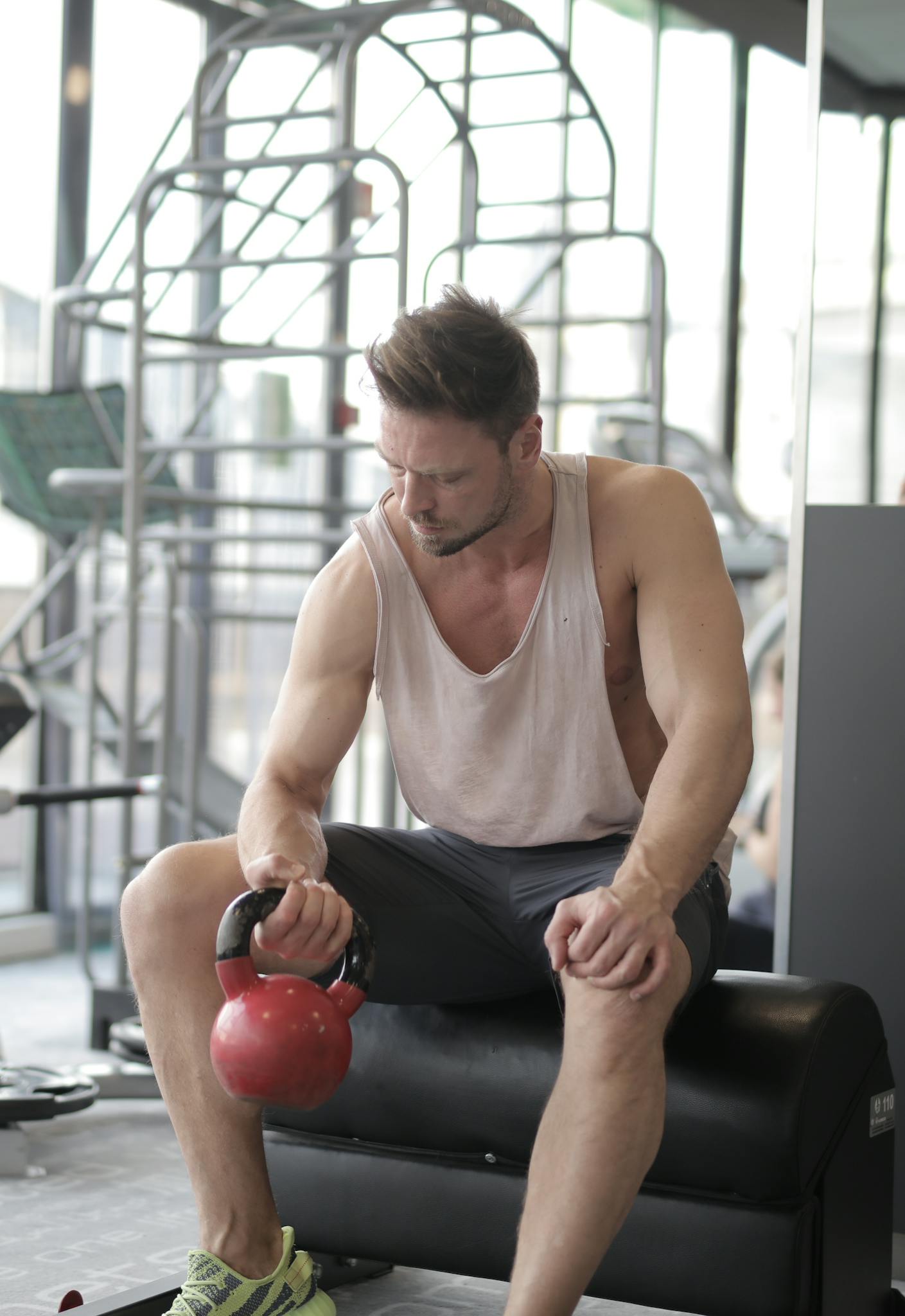 An athletic man in a gym focuses on strength training with a red kettlebell.