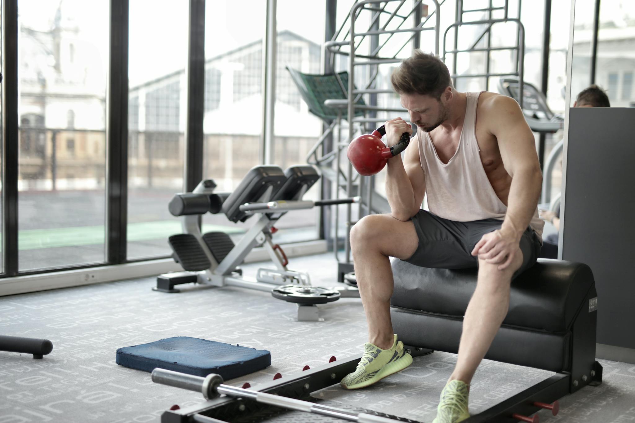 Young man performing bicep curls with kettlebell in a well-equipped gym.
